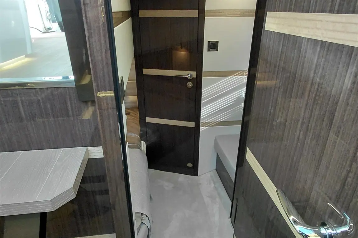 Interior view of a luxury yacht cabin with dark wood finishes, a door, and a small table on the left.